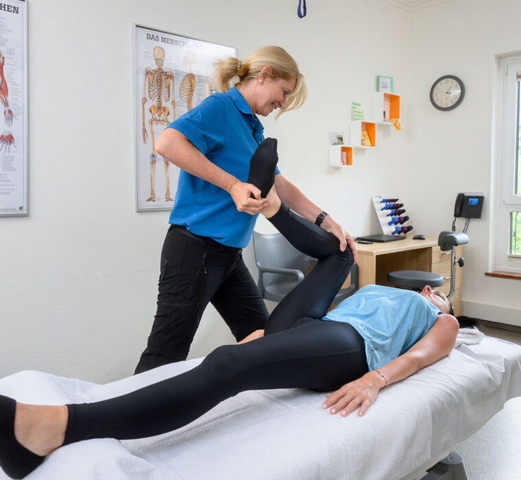 Therapeutin mobilisiert das Bein einer Patientin im Behandlungsraum des Bärenhofs zur Verbesserung der Gelenkfunktion und Schmerzlinderung.