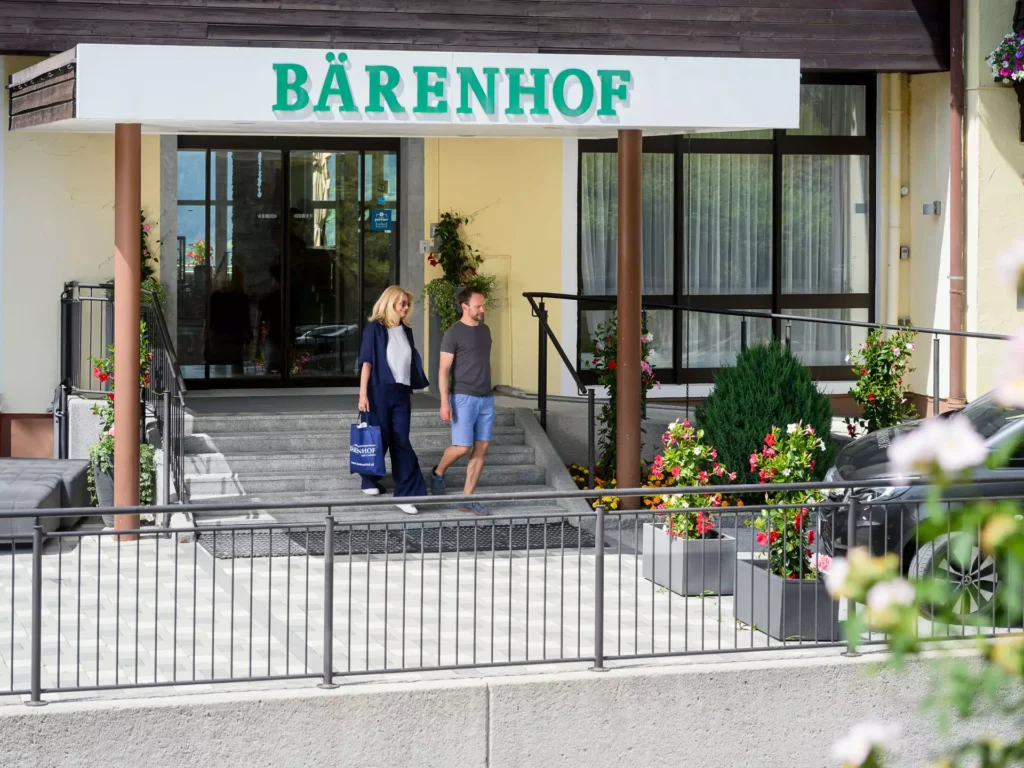 Zwei Personen verlassen den Haupteingang des Bärenhofs in Bad Gastein – gepflegter Eingangsbereich mit Blumen und barrierefreiem Zugang.