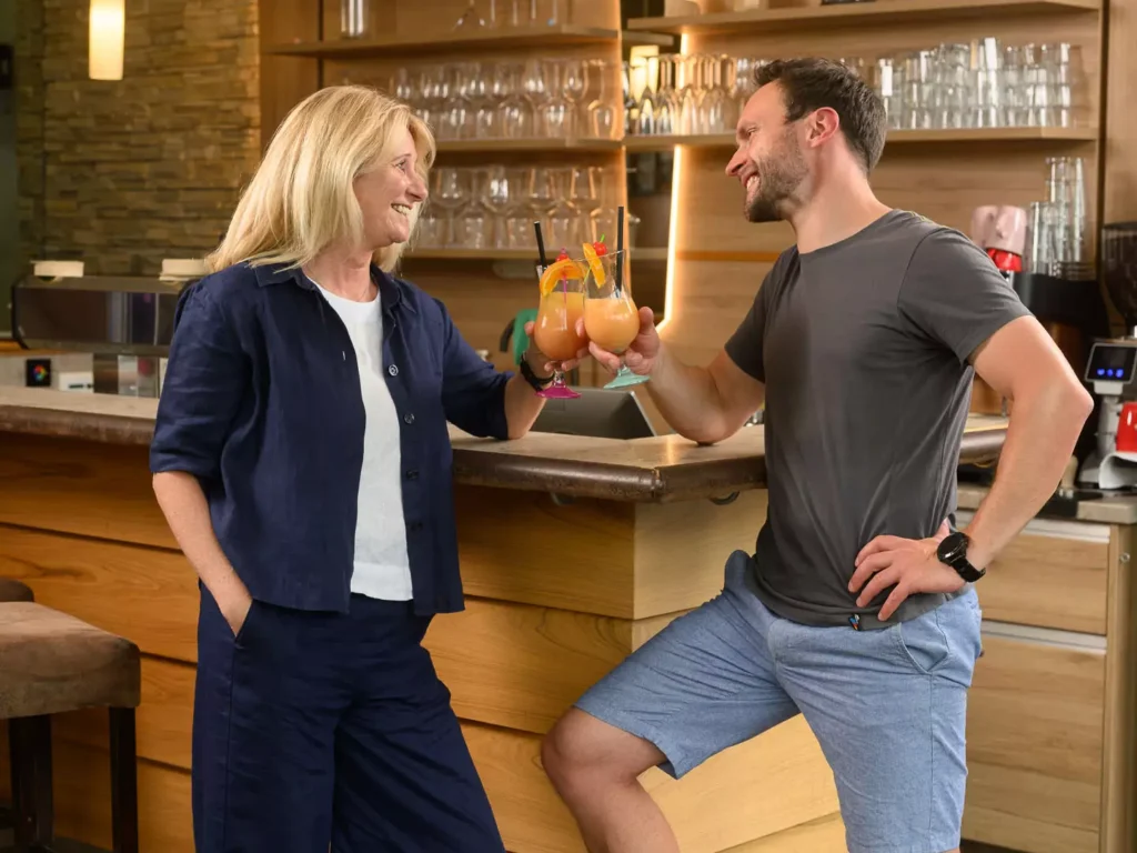 Zwei Gäste stoßen mit fruchtigen Cocktails an der Bar im Felsencafé des Bärenhofs Bad Gastein an – entspannte Stimmung in stilvollem Ambiente.