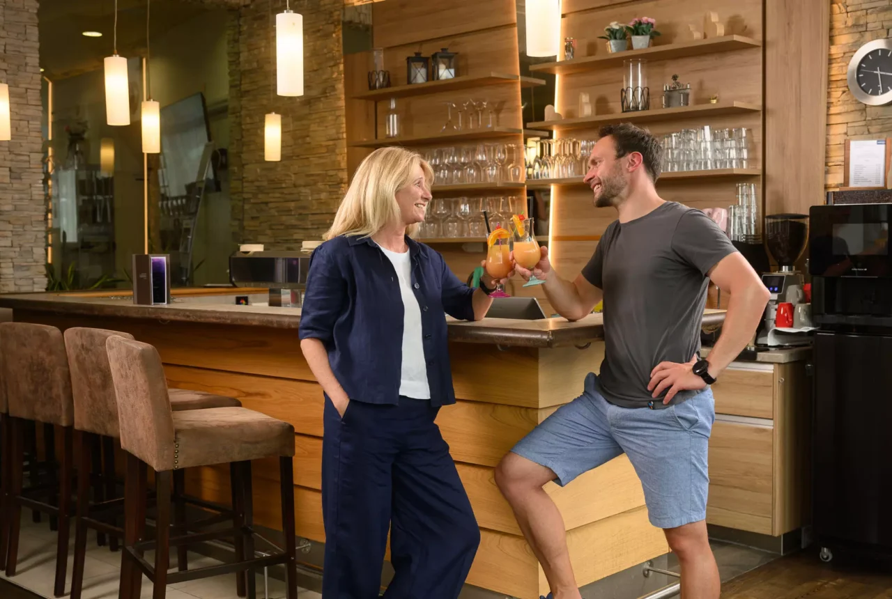 Zwei Gäste stoßen mit fruchtigen Cocktails an der Bar im Felsencafé des Bärenhofs Bad Gastein an – entspannte Stimmung in stilvollem Ambiente.