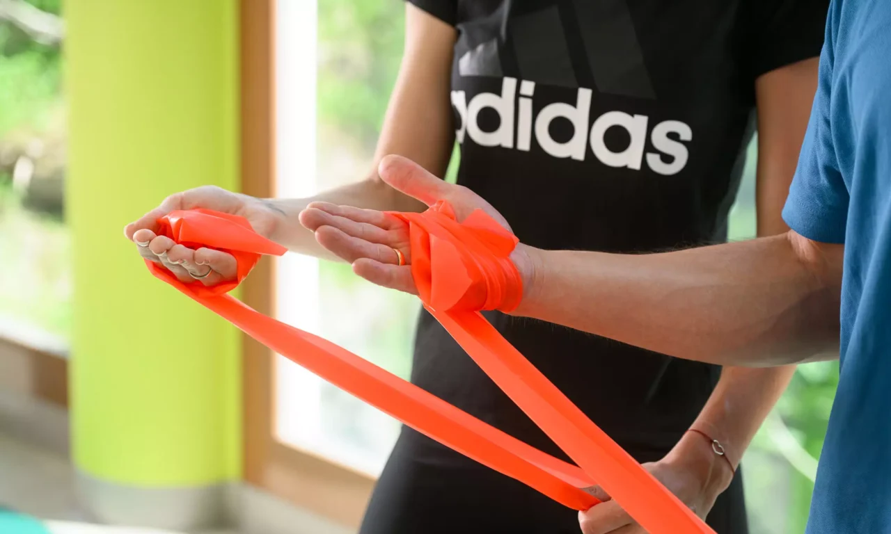 Detailaufnahme: Therapeut zeigt Patientin die korrekte Handhaltung mit einem Theraband zur Vorbereitung auf eine physiotherapeutische Übung.