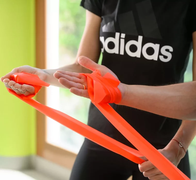Detailaufnahme: Therapeut zeigt Patientin die korrekte Handhaltung mit einem Theraband zur Vorbereitung auf eine physiotherapeutische Übung.