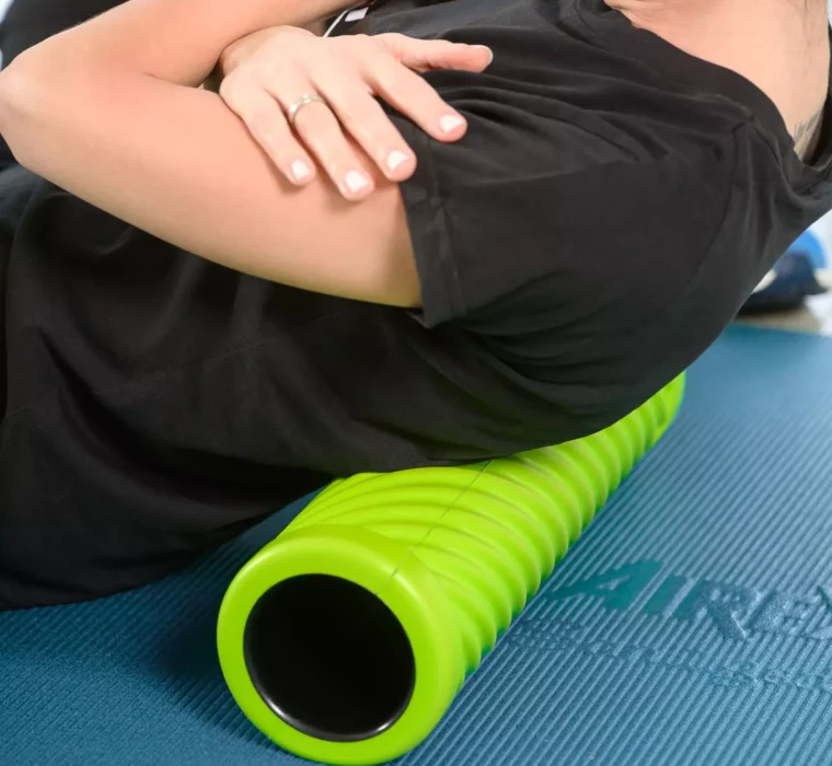 Nahaufnahme einer therapeutischen Rückenübung mit Faszienrolle zur Mobilisation der Brustwirbelsäule auf einer Gymnastikmatte.