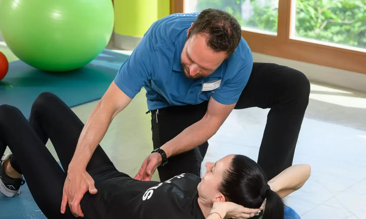 Physiotherapeut unterstützt Frau bei Rückenübung mit Faszienrolle im hauseigenen Gymnastikraum