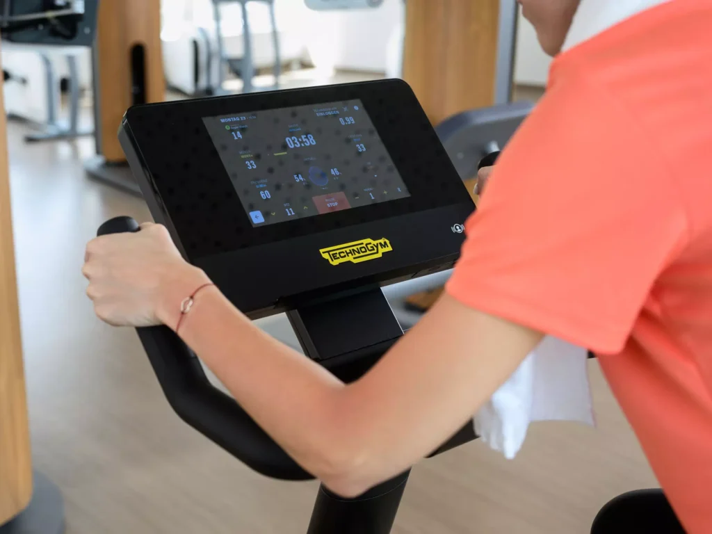 Patientin trainiert im modernen Fitnessbereich des Bärenhofs auf einem Technogym-Ergometer mit digitalem Display.