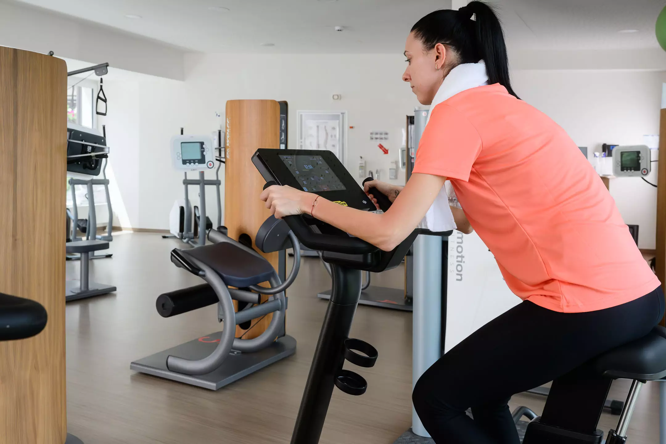 Patientin trainiert im modernen Fitnessbereich des Bärenhofs auf einem Technogym-Ergometer mit digitalem Display.
