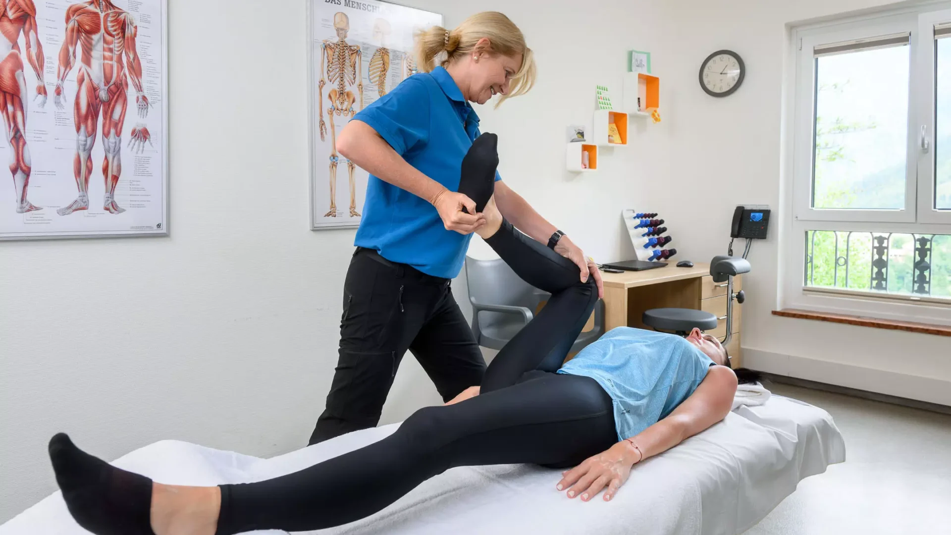 Therapeutin mobilisiert das Bein einer Patientin im Behandlungsraum des Bärenhofs zur Verbesserung der Gelenkfunktion und Schmerzlinderung.