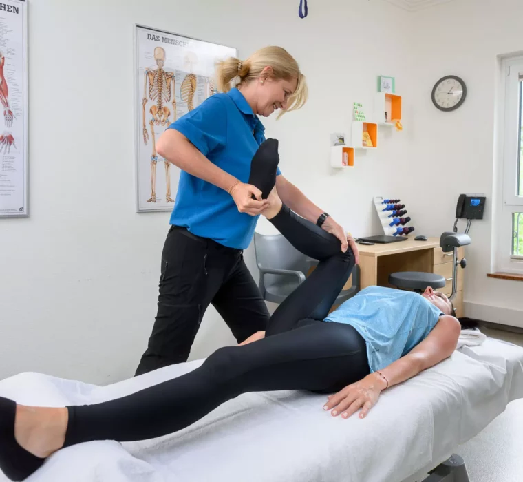 Therapeutin mobilisiert das Bein einer Patientin im Behandlungsraum des Bärenhofs zur Verbesserung der Gelenkfunktion und Schmerzlinderung.