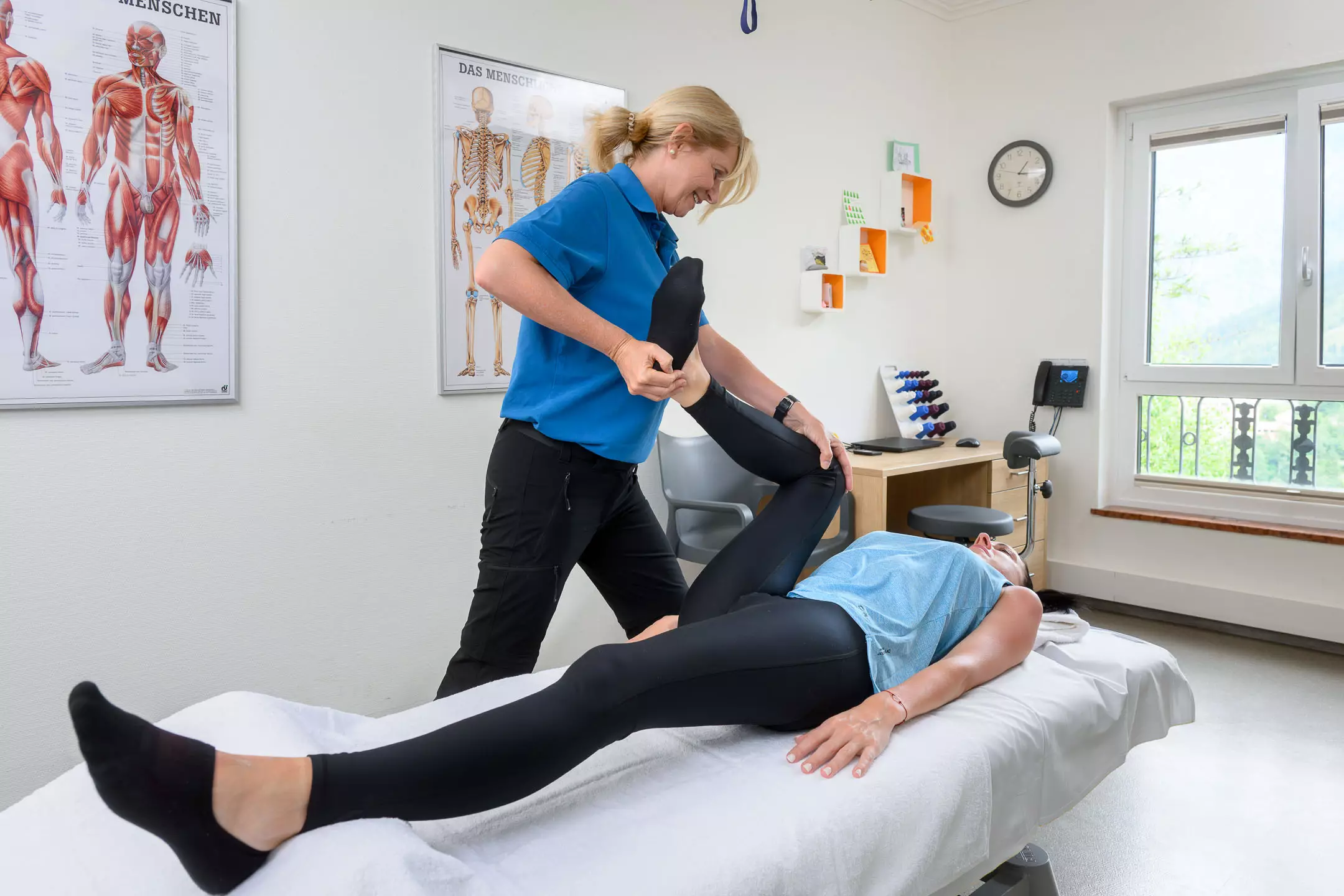 Therapeutin mobilisiert das Bein einer Patientin im Behandlungsraum des Bärenhofs zur Verbesserung der Gelenkfunktion und Schmerzlinderung.