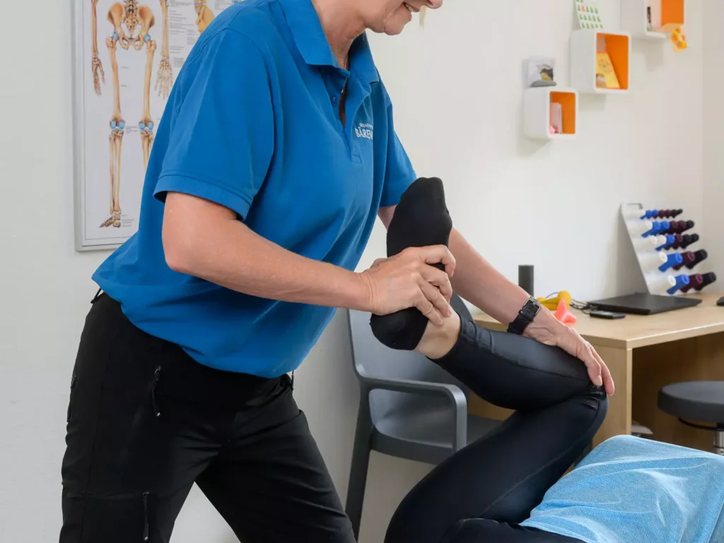 Therapeutin mobilisiert das Bein einer Patientin im Behandlungsraum des Bärenhofs zur Verbesserung der Gelenkfunktion und Schmerzlinderung.