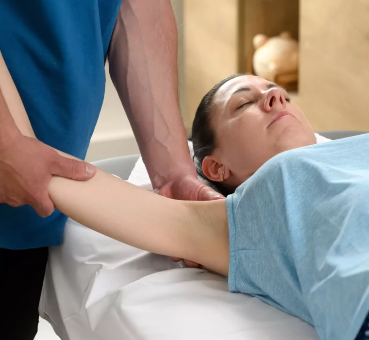 Patientin liegt entspannt auf der Behandlungsliege, während ein Therapeut im Bärenhof die Schulter- und Armmobilisation zur Schmerzlinderung durchführt.