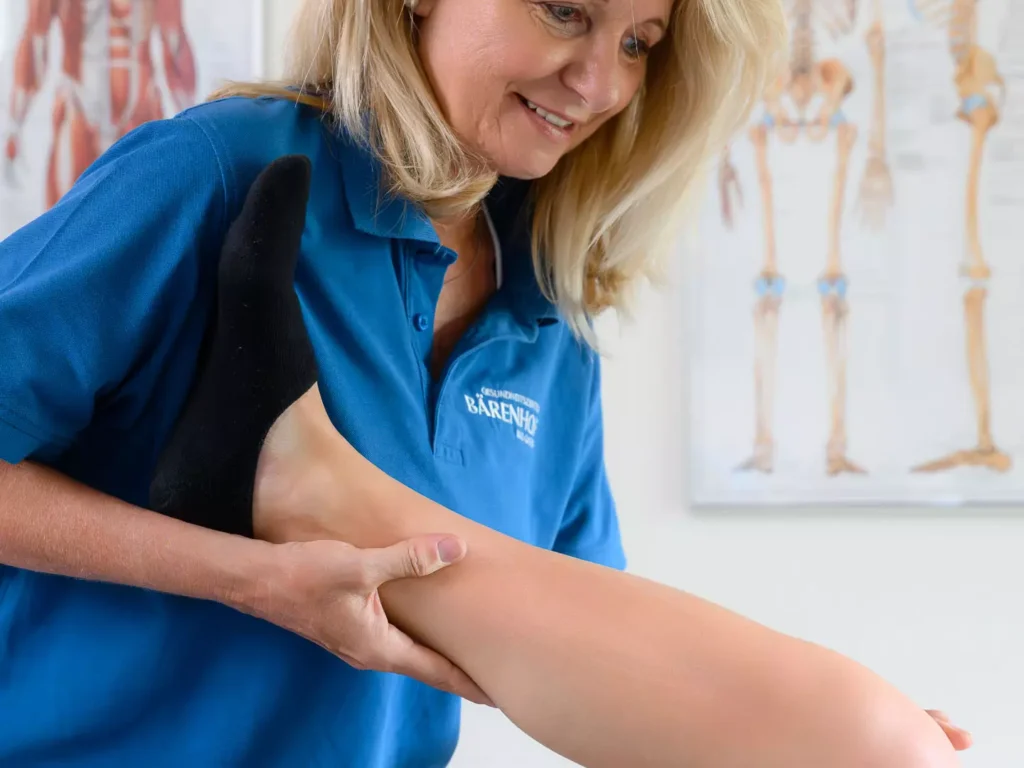 Therapeutin im Bärenhof mobilisiert mit einem Lächeln das Bein einer Patientin – gezielte Behandlung zur Förderung von Beweglichkeit und Schmerzlinderung.