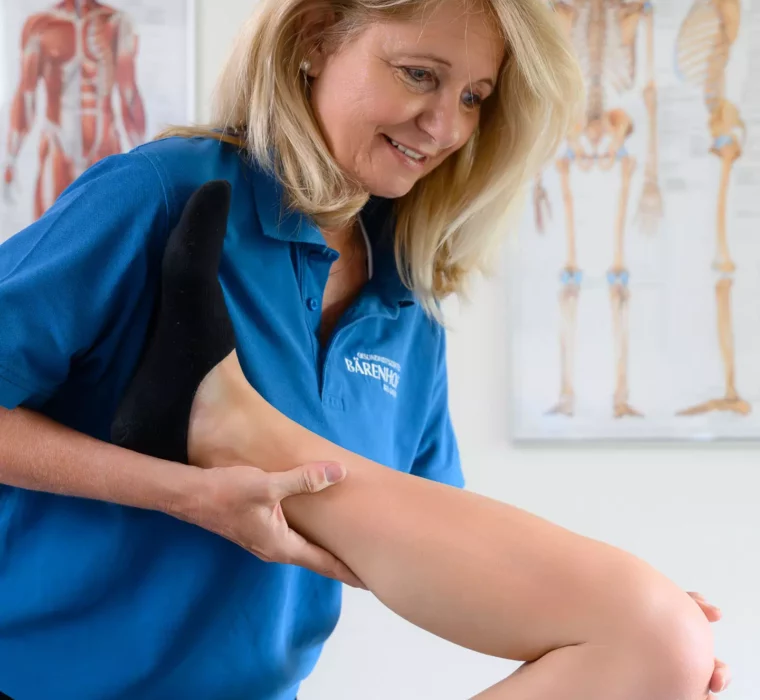 Therapeutin im Bärenhof mobilisiert mit einem Lächeln das Bein einer Patientin – gezielte Behandlung zur Förderung von Beweglichkeit und Schmerzlinderung.