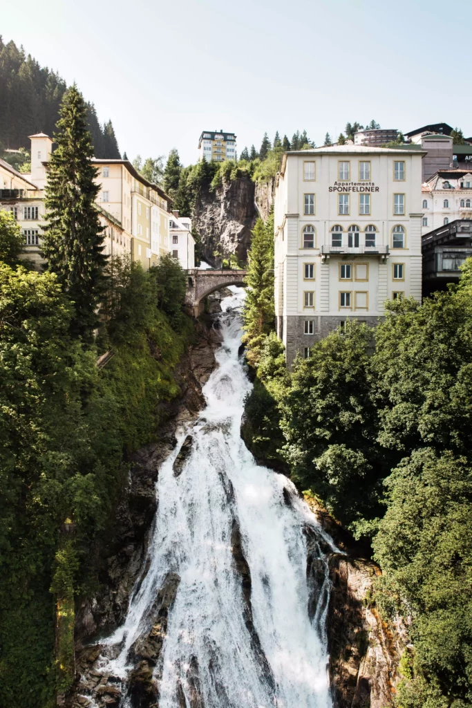 Wasserfall in Bad Gastein umgeben von grünen Bäumen und historischen Gebäuden mit Brücke und Appartementhaus Sponfeldner