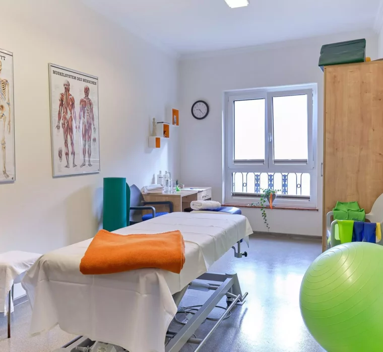 Behandlungsraum im Gesundheitszentrum Bärenhof Bad Gastein mit Liege, Anatomiepostern und Therapiegeräten für Kuraufenthalt
