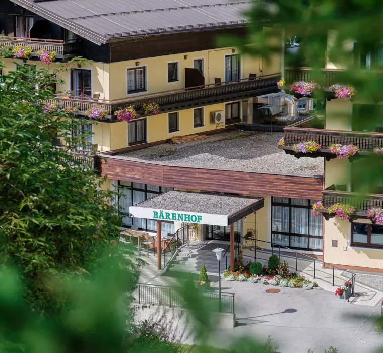 Eingang des Kurhotels Bärenhof in Bad Gastein mit Blumen geschmückten Balkonen und parkenden Autos, umgeben von grüner Natur