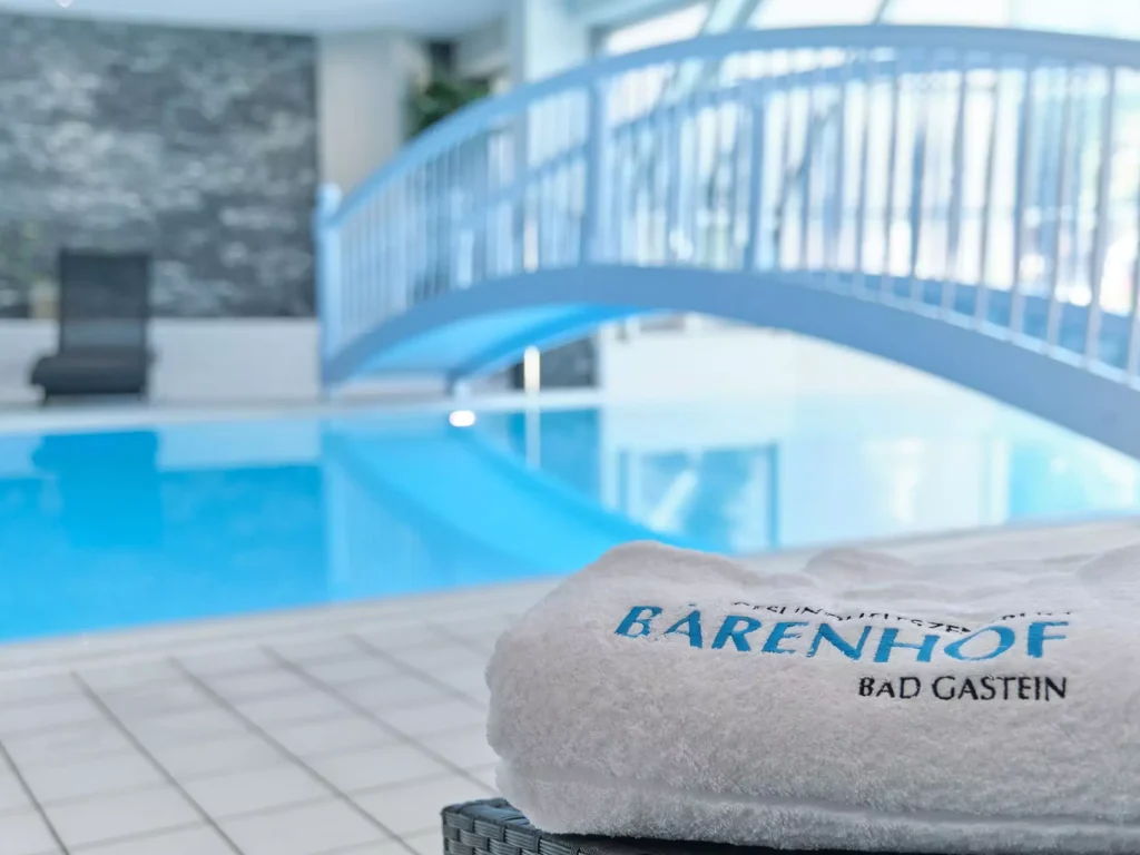 Weißes Handtuch mit Bärenhof Bad Gastein Schriftzug am Rand eines hellen Hallenbads mit blauer Brücke im Hintergrund