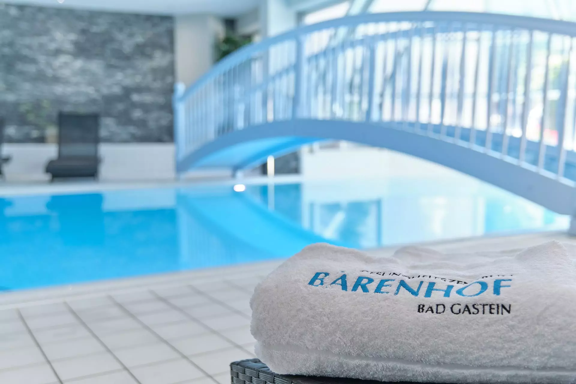 Weißes Handtuch mit Bärenhof Bad Gastein Schriftzug am Rand eines hellen Hallenbads mit blauer Brücke im Hintergrund