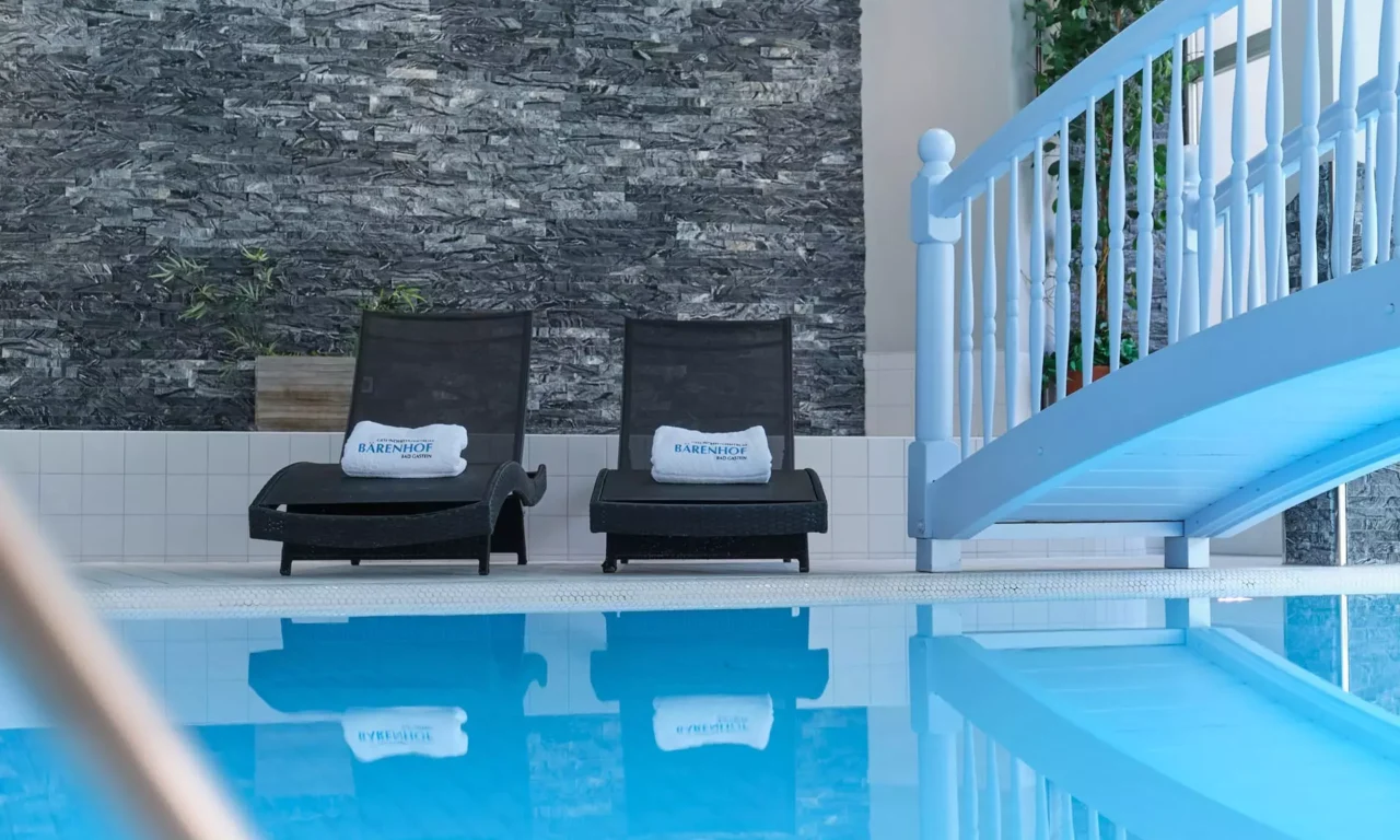 Innenaufnahme des Hallenbads im Gesundheitszentrum Kurhotel Bärenhof Bad Gastein mit Liegestühlen und Brücke über das Wasser