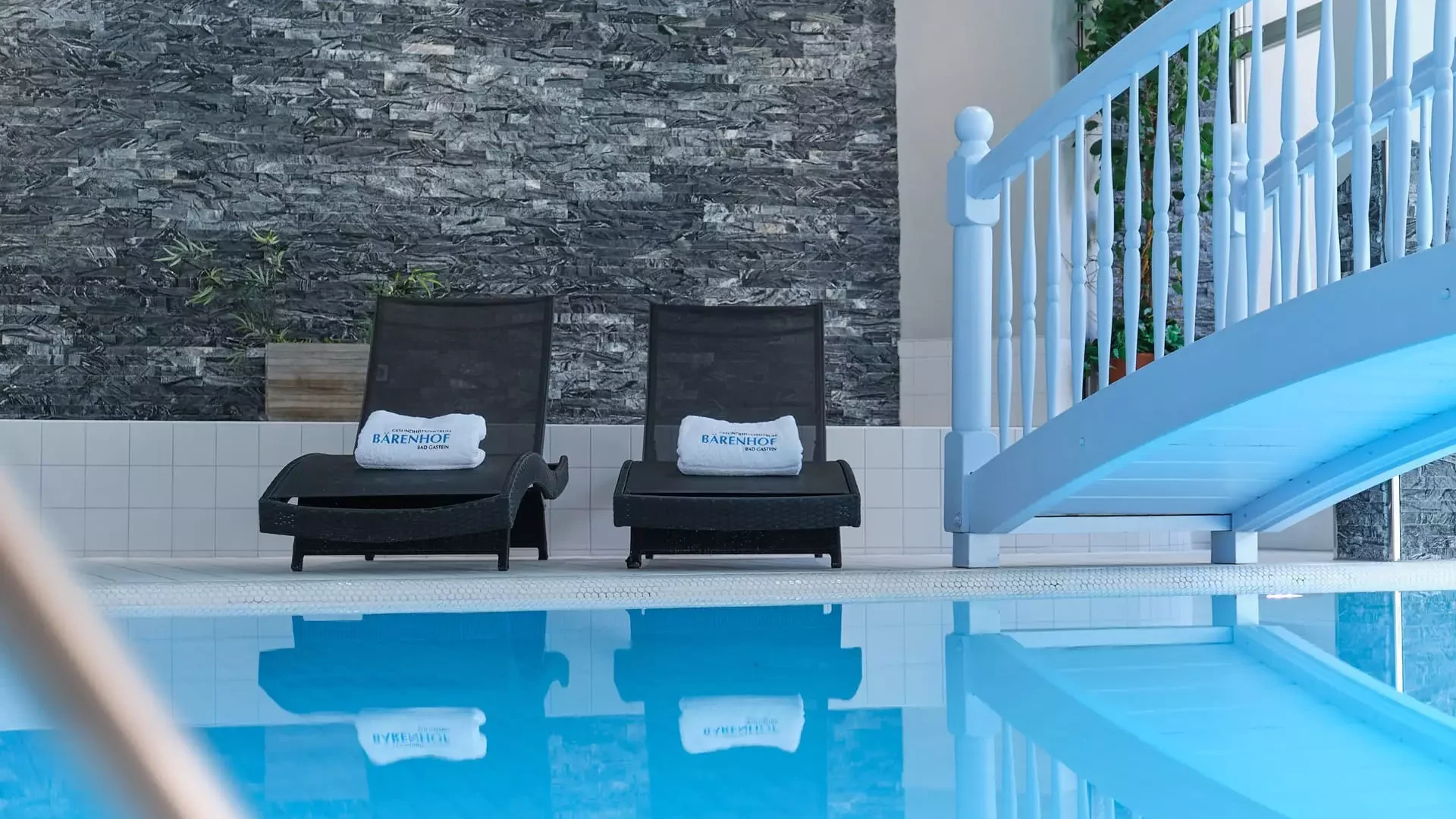 Innenaufnahme des Hallenbads im Gesundheitszentrum Kurhotel Bärenhof Bad Gastein mit Liegestühlen und Brücke über das Wasser