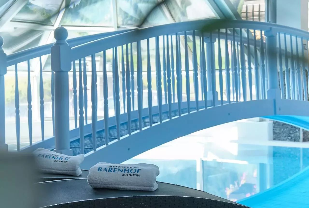 Innenaufnahme des Hallenbads im Gesundheitszentrum Kurhotel Bärenhof Bad Gastein mit Liegen und Brücke über das Wasser