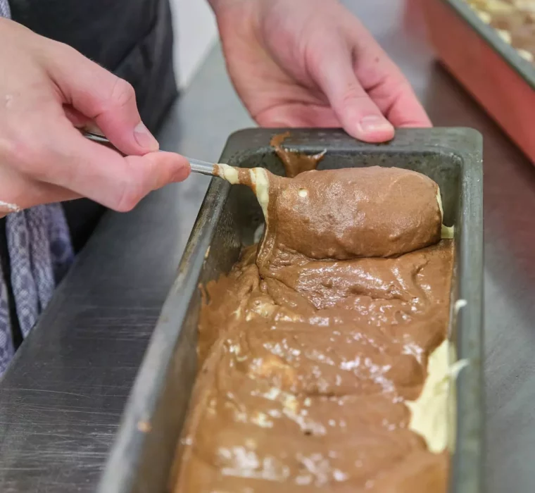 Hände verteilen Schokoladen- und Vanilleteig in einer Backform in der Küche des Gesundheitszentrums Bärenhof Bad Gastein.