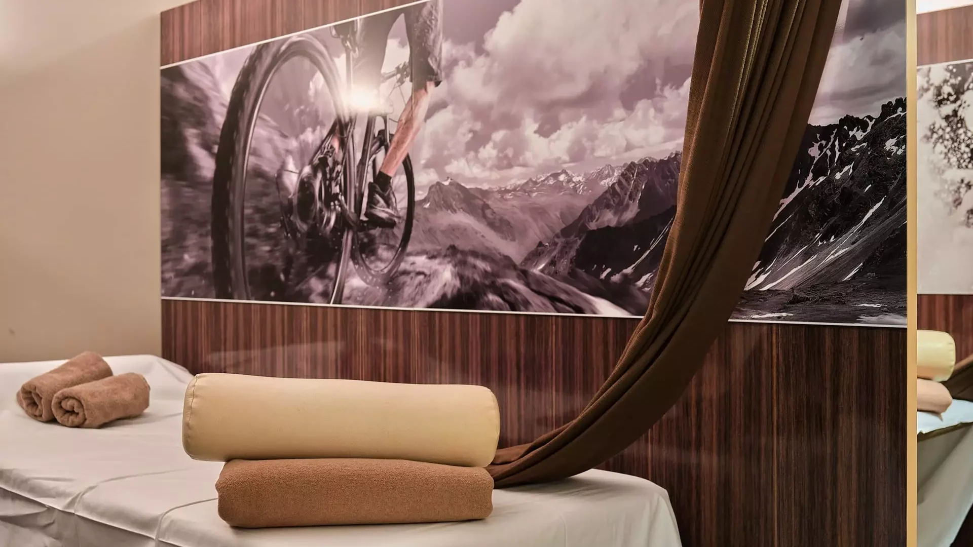 Behandlungsraum im Gesundheitszentrum Bärenhof Bad Gastein mit Massageliege, Handtüchern und Bergpanorama-Fotowand