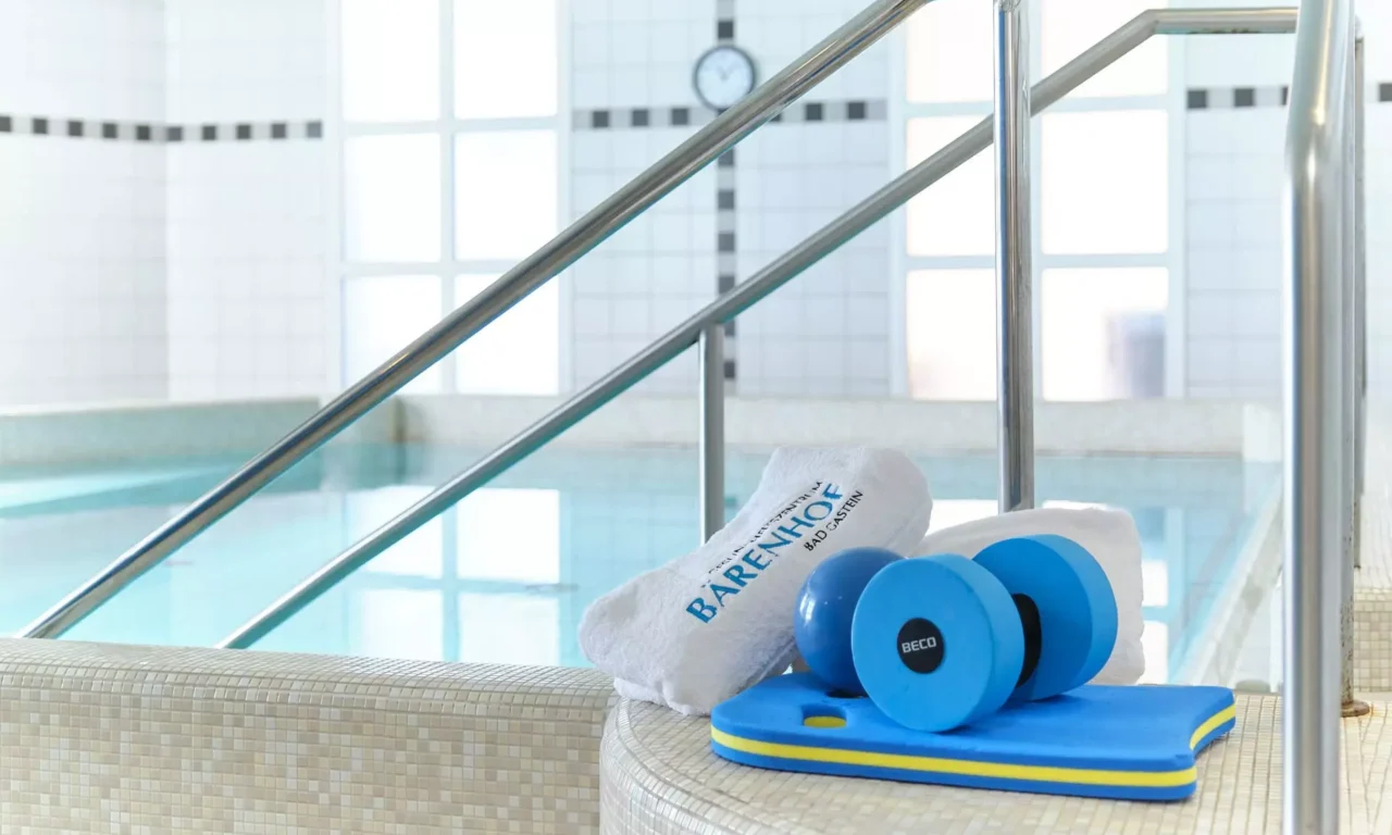 Innenaufnahme eines Pools im Gesundheitszentrum Bärenhof Bad Gastein mit Handtüchern, blauen Hanteln und Schwimmbrett am