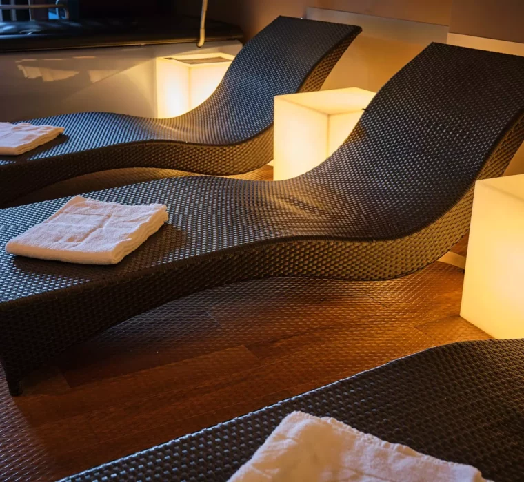 Dunkle Relaxliegen mit weißen Handtüchern und warm leuchtenden Würfellampen im Wellnessbereich des Gesundheitszentrums