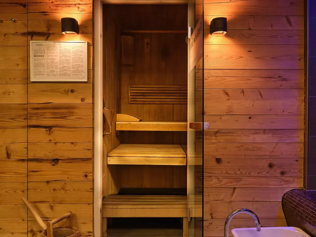 Holzsauna mit offener Glastür, Holzeimer mit Kelle und zwei weißen Fußbecken im Wellnessbereich des Bärenhof Bad Gastein
