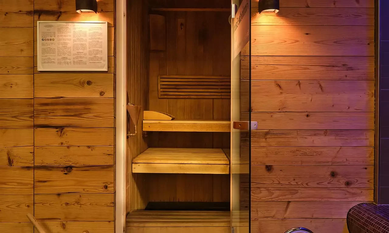 Holzsauna mit offener Glastür, Holzeimer mit Kelle und zwei weißen Fußbecken im Wellnessbereich des Bärenhof Bad Gastein