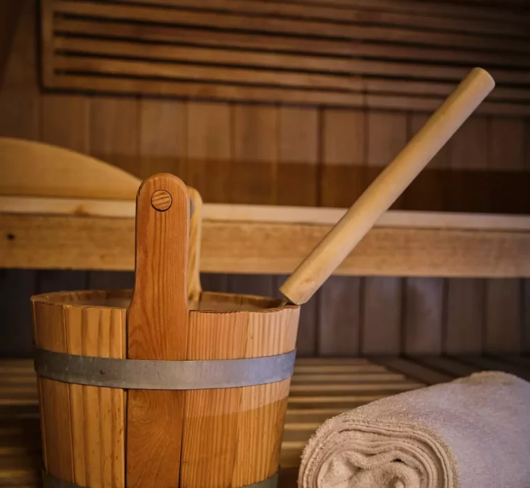 Holzeimer mit Kelle und zusammengerolltes Handtuch in einer Sauna im Gesundheitszentrum Bärenhof Bad Gastein