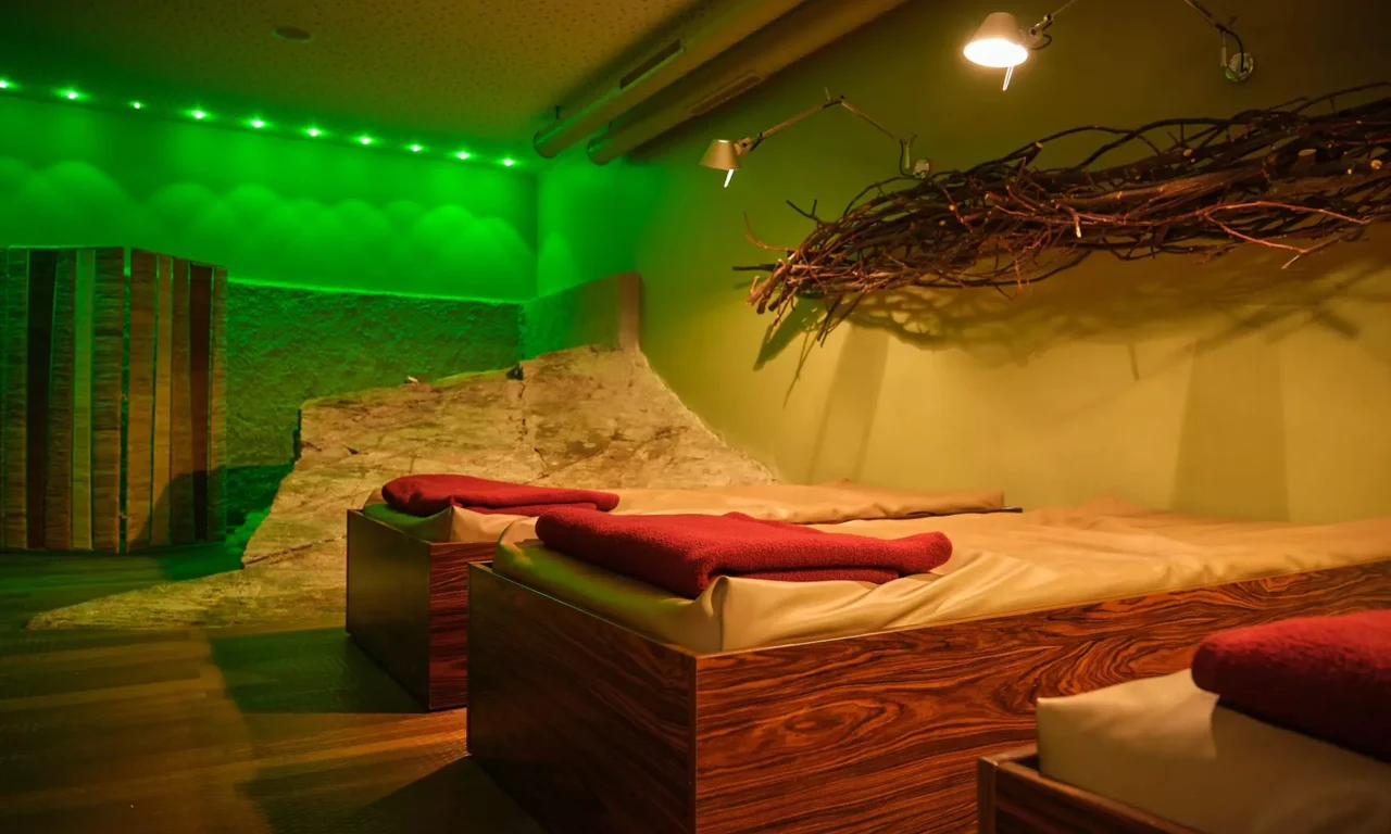Ruheraum im Gesundheitszentrum Bärenhof Bad Gastein mit Liegen, roten Handtüchern und grüner Ambientebeleuchtung