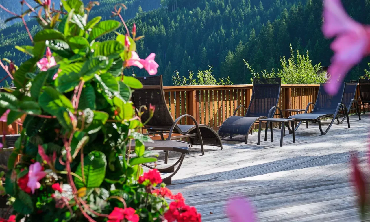 Sonnige Holzterrasse mit Liegestühlen und bunten Blumen vor bewaldeten Bergen im Gesundheitszentrum Bärenhof Bad Gastein