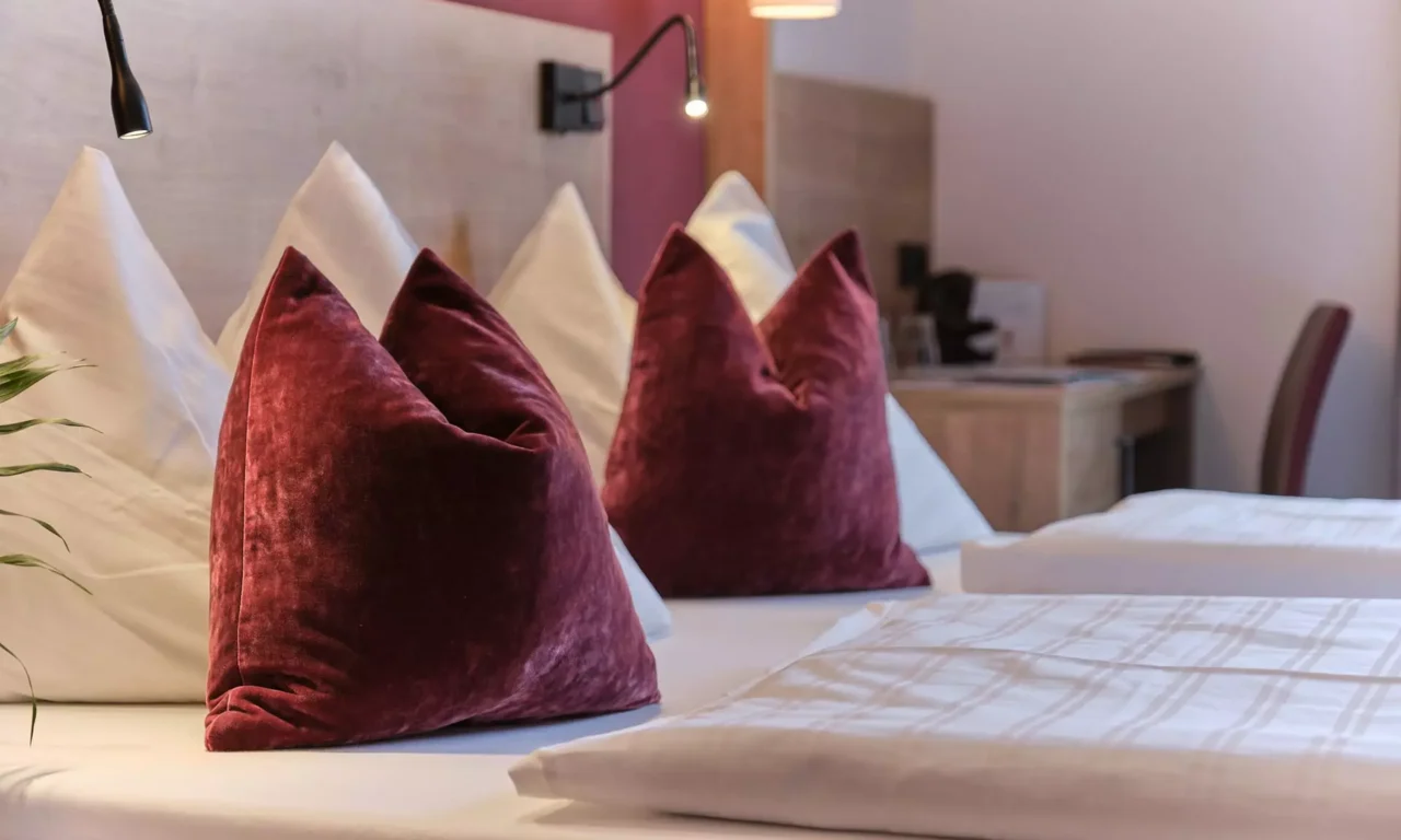 Gemütliches Hotelzimmer im Gesundheitszentrum Bärenhof Bad Gastein mit weißen und roten Kissen auf dem Bett und Leselampen.