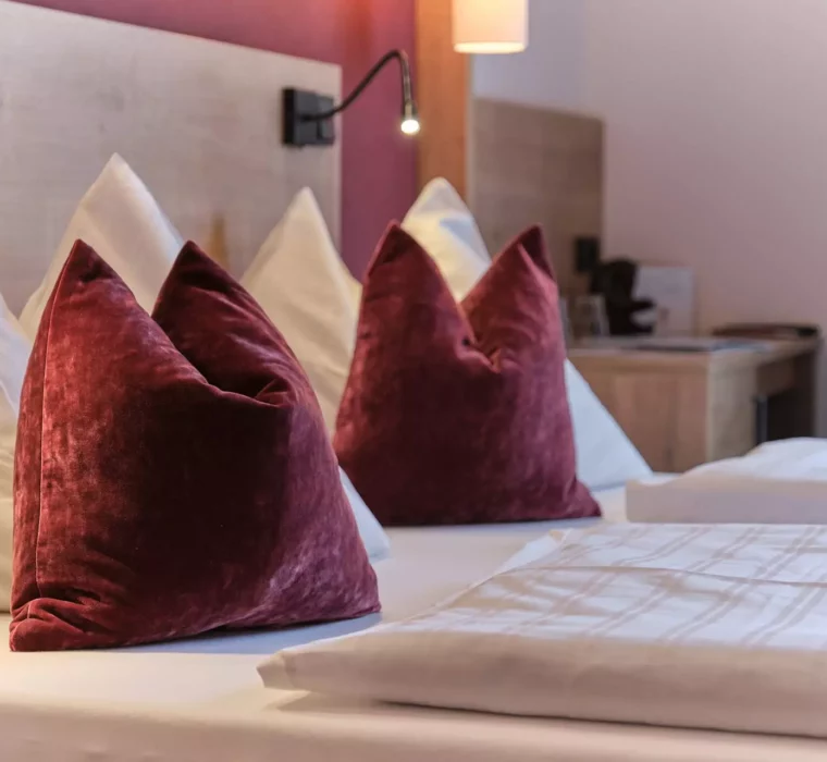 Gemütliches Hotelzimmer im Gesundheitszentrum Bärenhof Bad Gastein mit weißen und roten Kissen auf dem Bett und Leselampen.