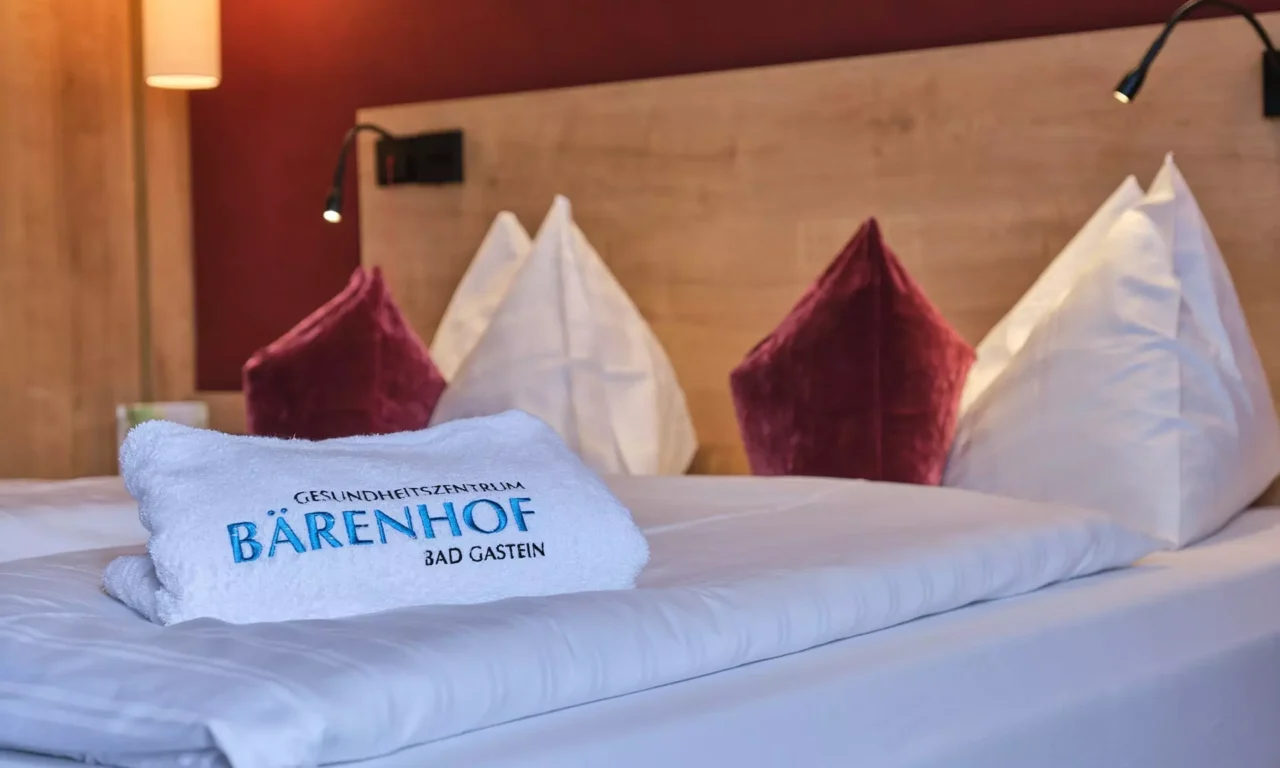 Bett mit weißen und roten Kissen, darauf ein Handtuch mit Stickerei Gesundheitszentrum Bärenhof Bad Gastein