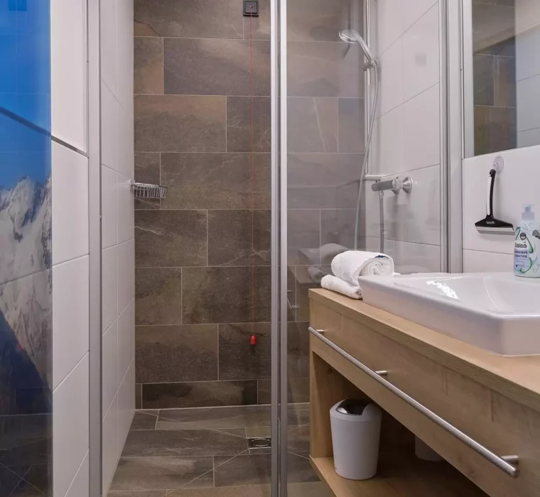 Modernes Badezimmer mit begehbarer Dusche, Holzwaschtisch, Handtüchern und Spiegel im Kurhotel Bärenhof Bad Gastein