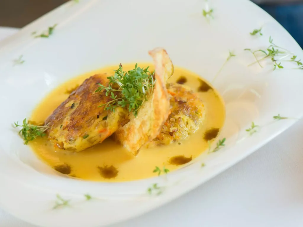 Zwei gebratene Gemüse-Laibchen in heller Sauce mit Kräutern auf weißem Teller im Gesundheitszentrum Bärenhof Bad Gastein