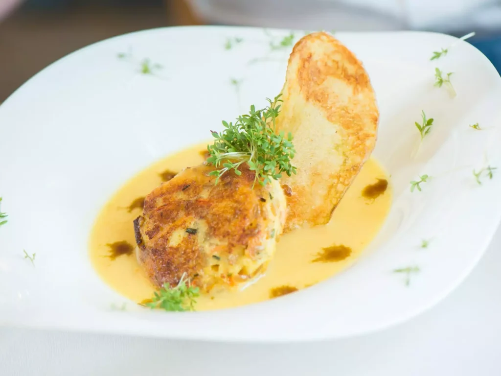 Gebratene Frikadelle mit Sauce, Kräutern und knusprigem Brotchip auf weißem Teller im Gesundheitszentrum Bärenhof Bad Gastein