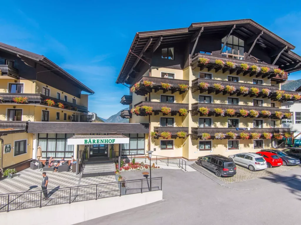 Außenansicht des Kurhotels Bärenhof in Bad Gastein mit Balkonen voller Blumen und Parkplätzen bei sonnigem Wetter