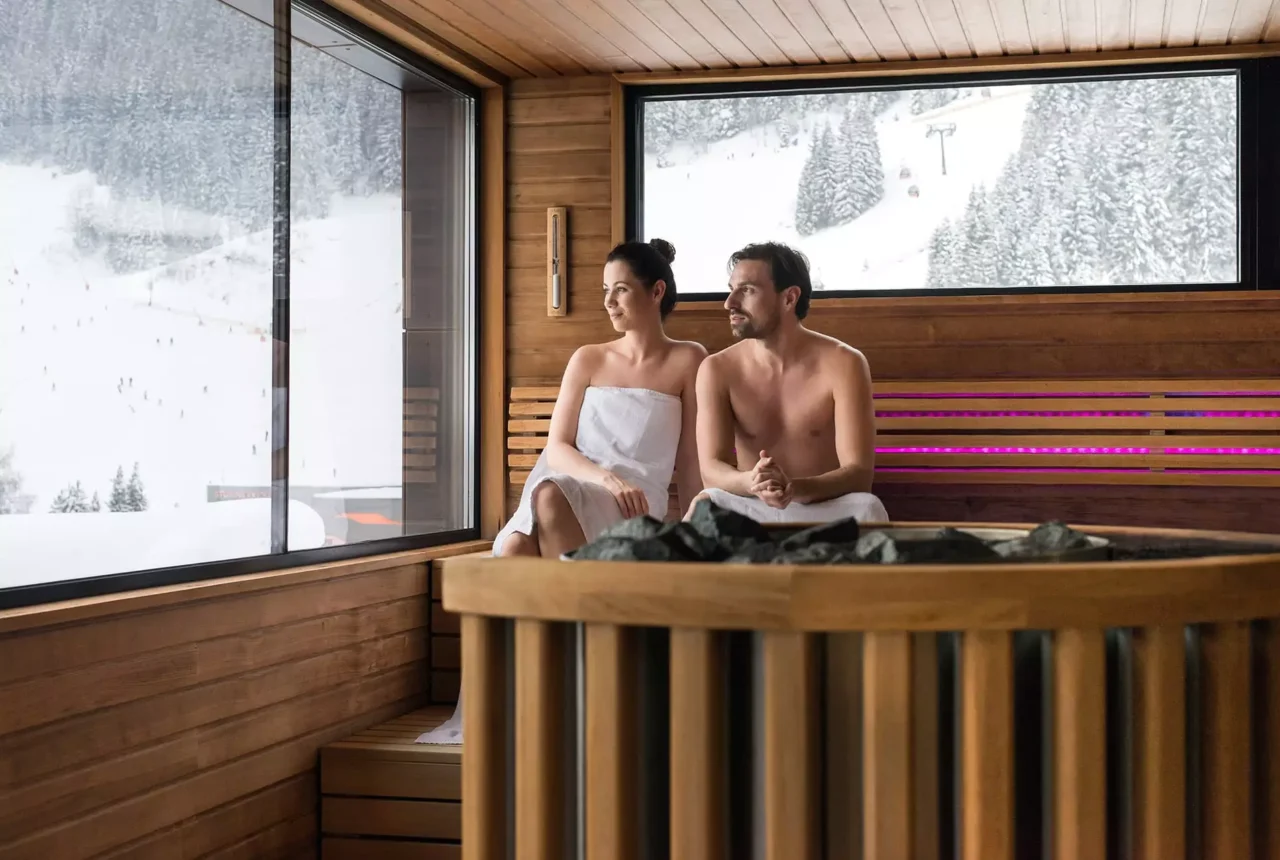 Paar entspannt in Sauna mit Blick auf verschneite Winterlandschaft im Gesundheitszentrum Bärenhof Bad Gastein