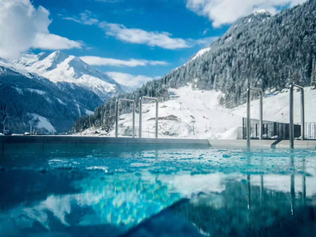 Außenpool mit klarem Wasser vor schneebedeckten Bergen und blauem Himmel im Gesundheitszentrum Bärenhof Bad Gastein