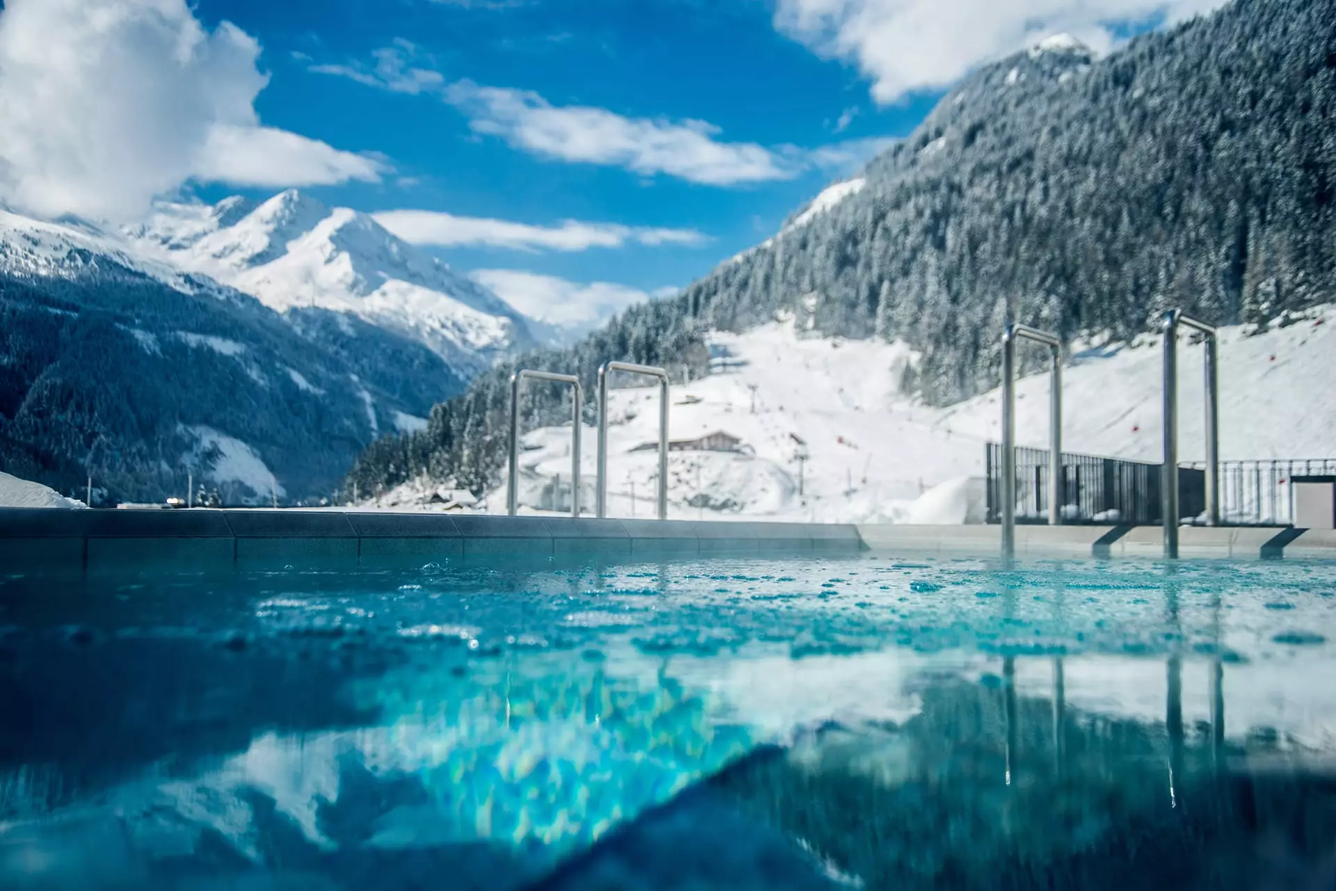 Außenpool mit klarem Wasser vor schneebedeckten Bergen und blauem Himmel im Gesundheitszentrum Bärenhof Bad Gastein