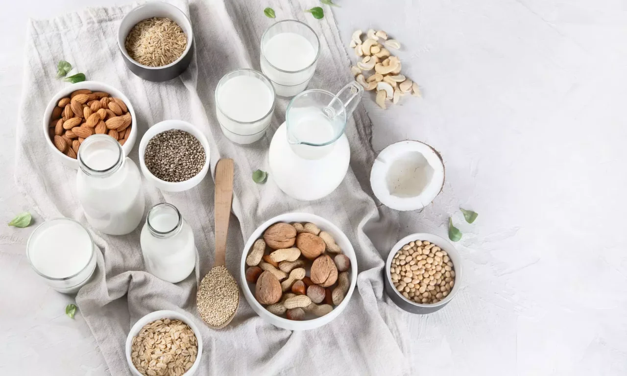 Verschiedene Nüsse, Samen, Getreide und pflanzliche Milch in Gläsern und Schalen auf hellem Tuch, gesunde Ernährung im