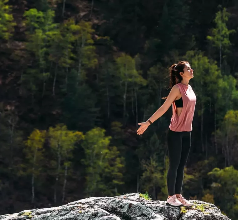 Frau steht mit offenen Armen auf Felsen vor bewaldetem Berg und genießt frische Luft und Natur in Bad Gastein