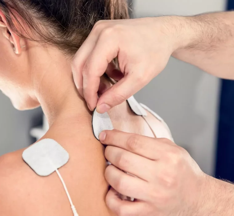 Therapeut bringt Elektroden zur Schmerztherapie am Nacken einer Patientin im Gesundheitszentrum Bärenhof Bad Gastein an.