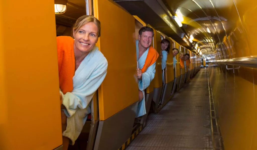 Mehrere Personen in Bademänteln lehnen aus gelben Türen eines langen Ganges im Gesundheitszentrum Bärenhof Bad Gastein