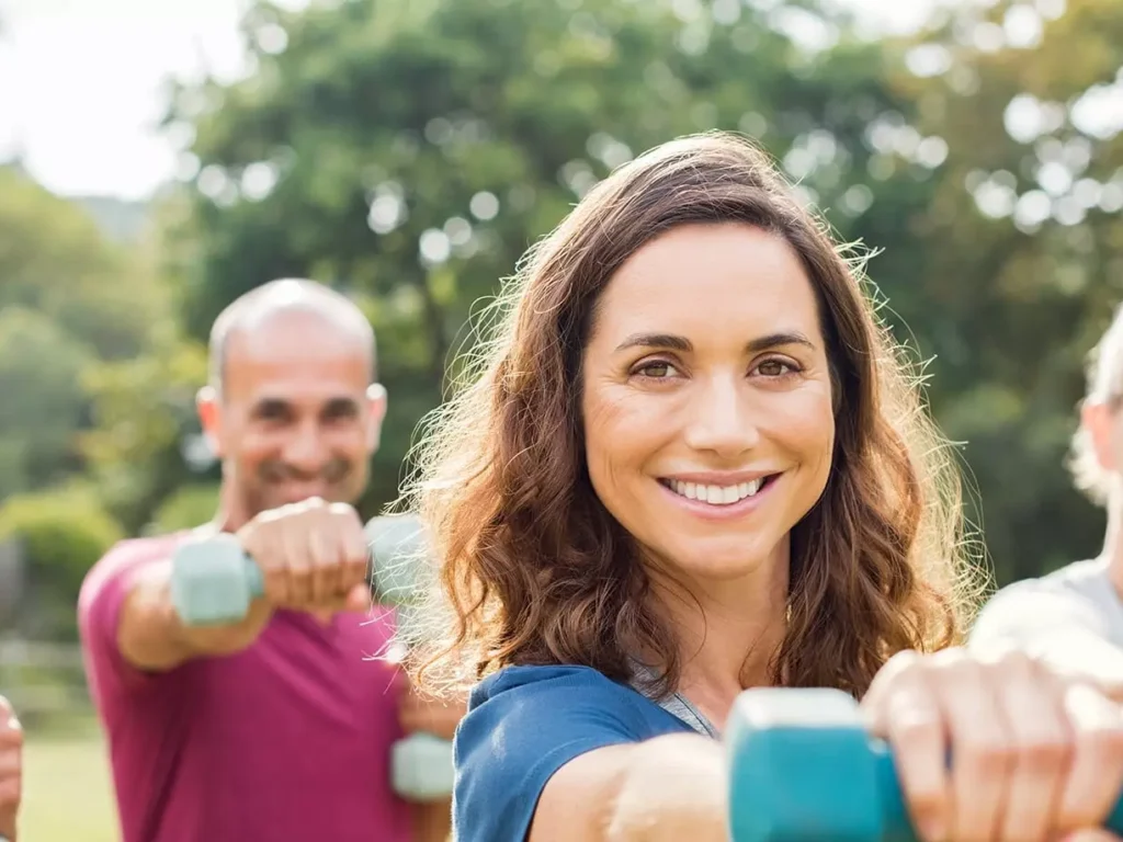 Vier lächelnde Erwachsene trainieren mit Hanteln im Freien in Bad Gastein für Rehabilitation und Erholung im Bärenhof